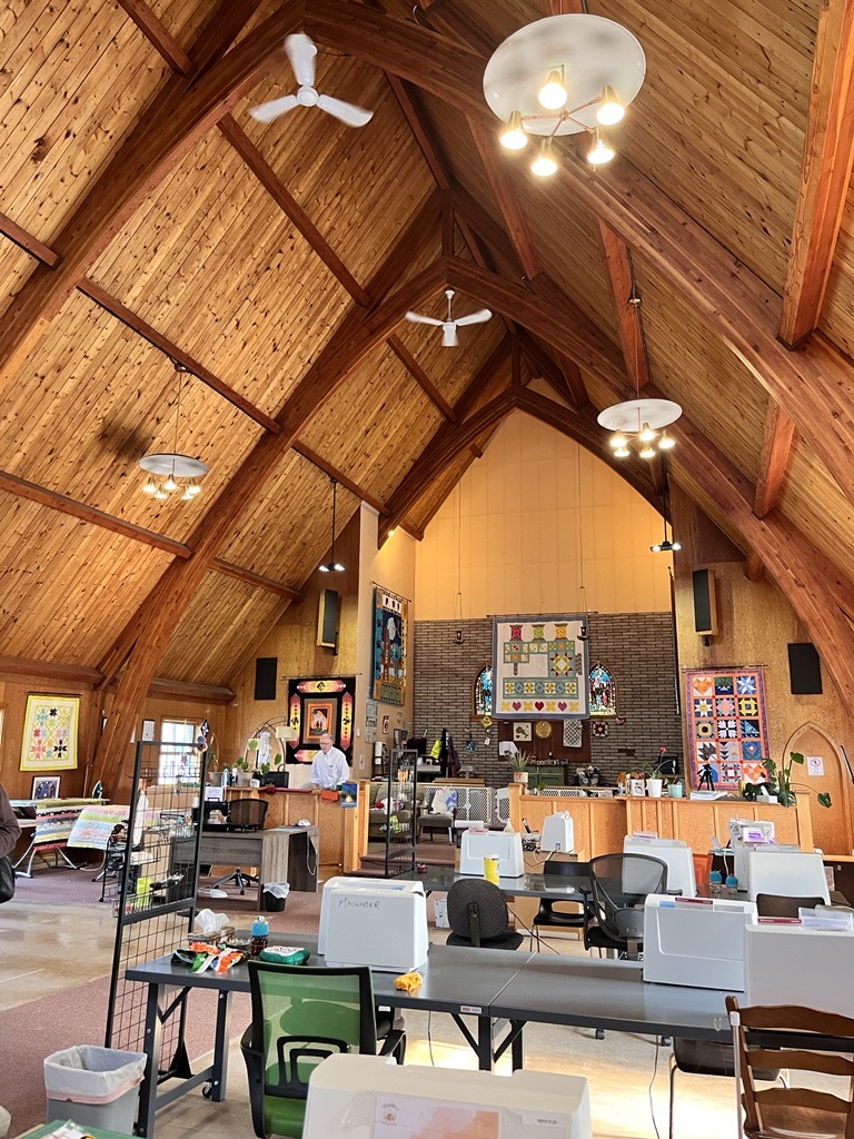 A re-purposed Anglican church with wooden rafters now houses several tables of sewing machines and quilts.