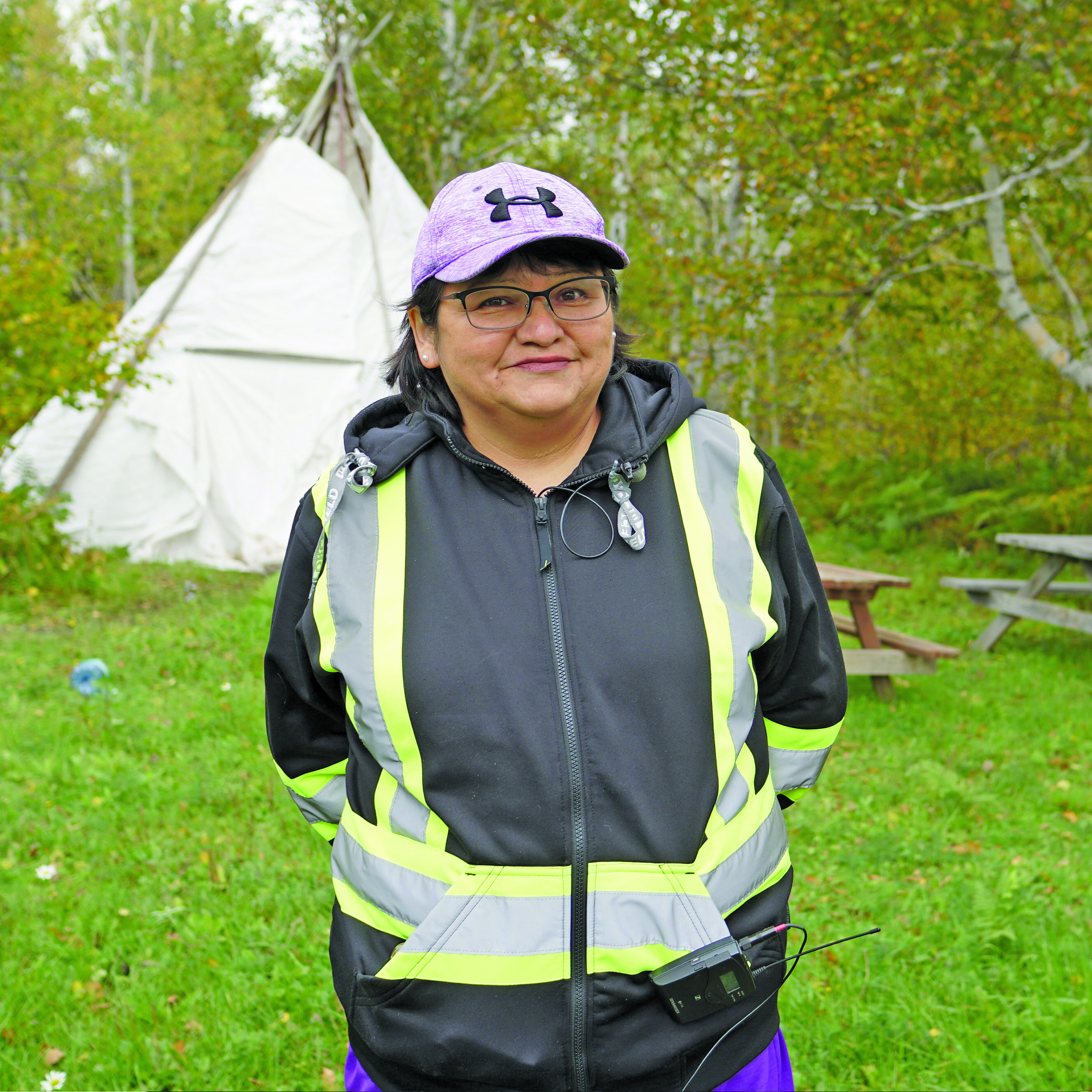 Person standing in a grassy area with a white structure behind them.