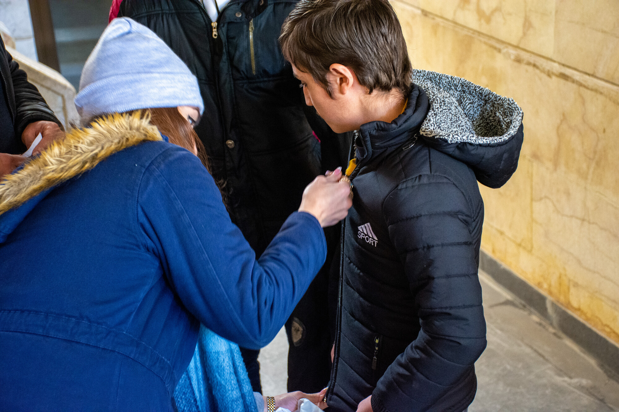 A kid tries on a new coat with assistance from his parent.