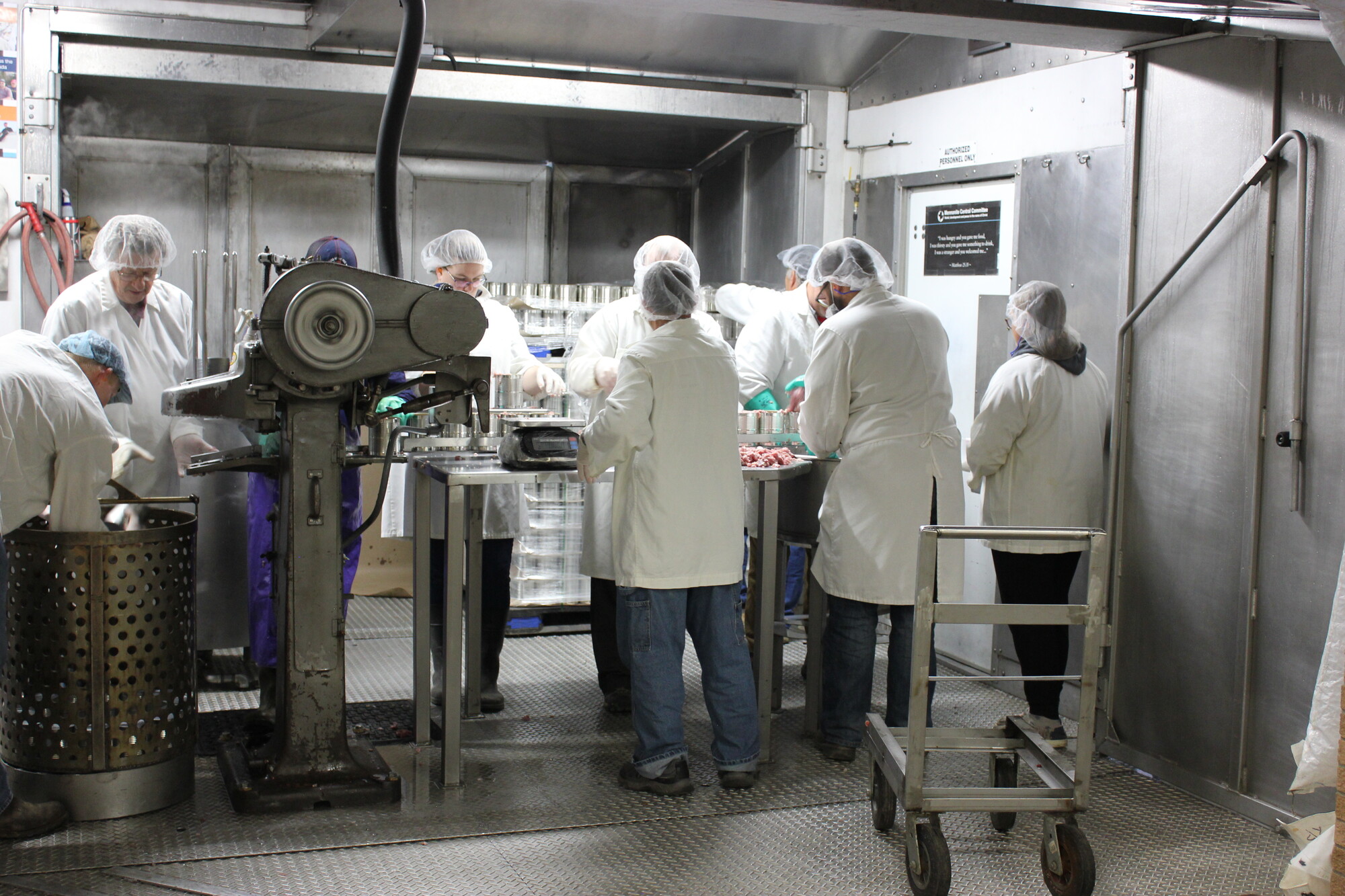 people wearing white coats and hair nets standing in rows, facing each other, on each side of a table