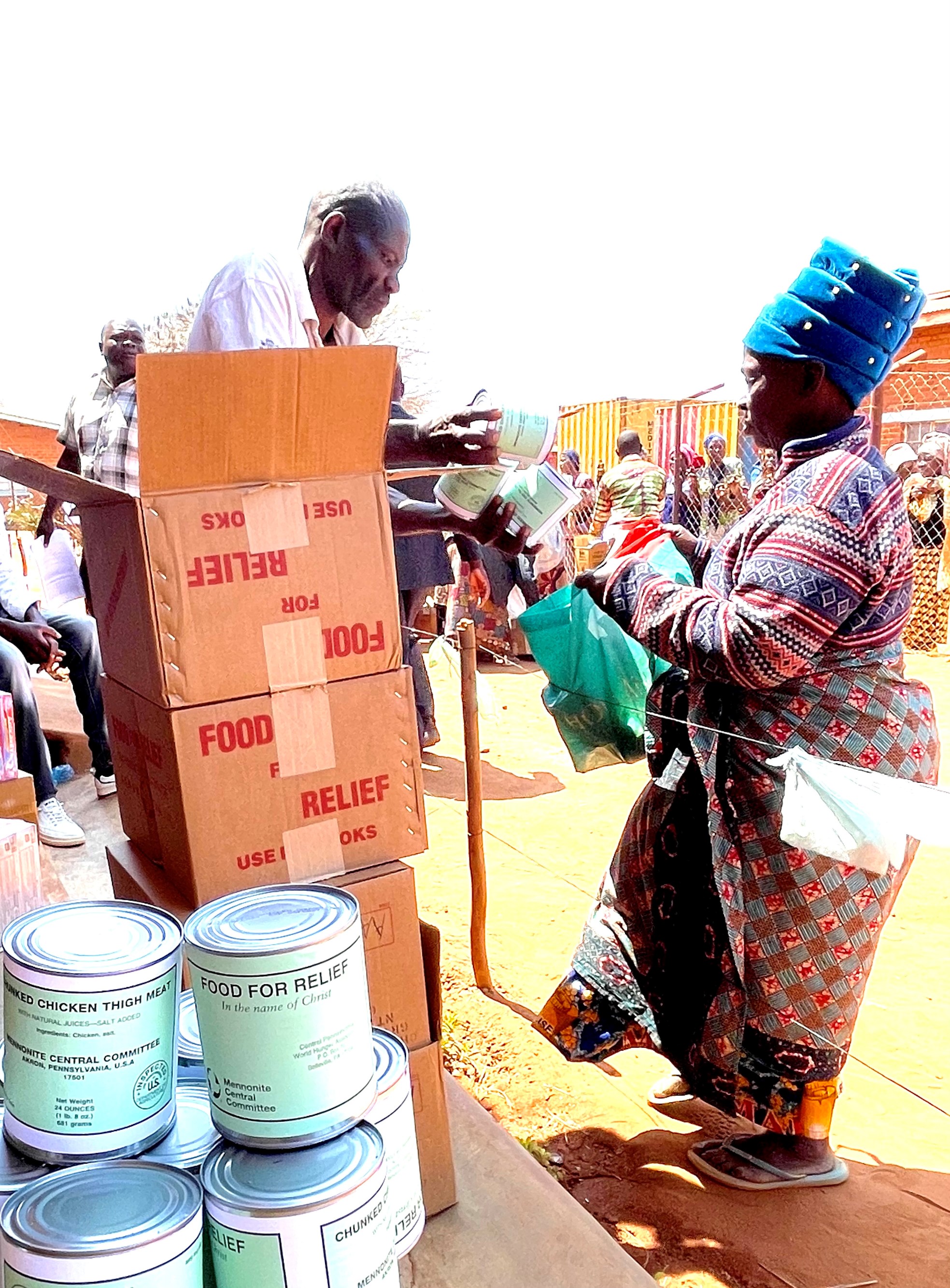 man standing behind a stack of boxes hands cans of meat to a woman