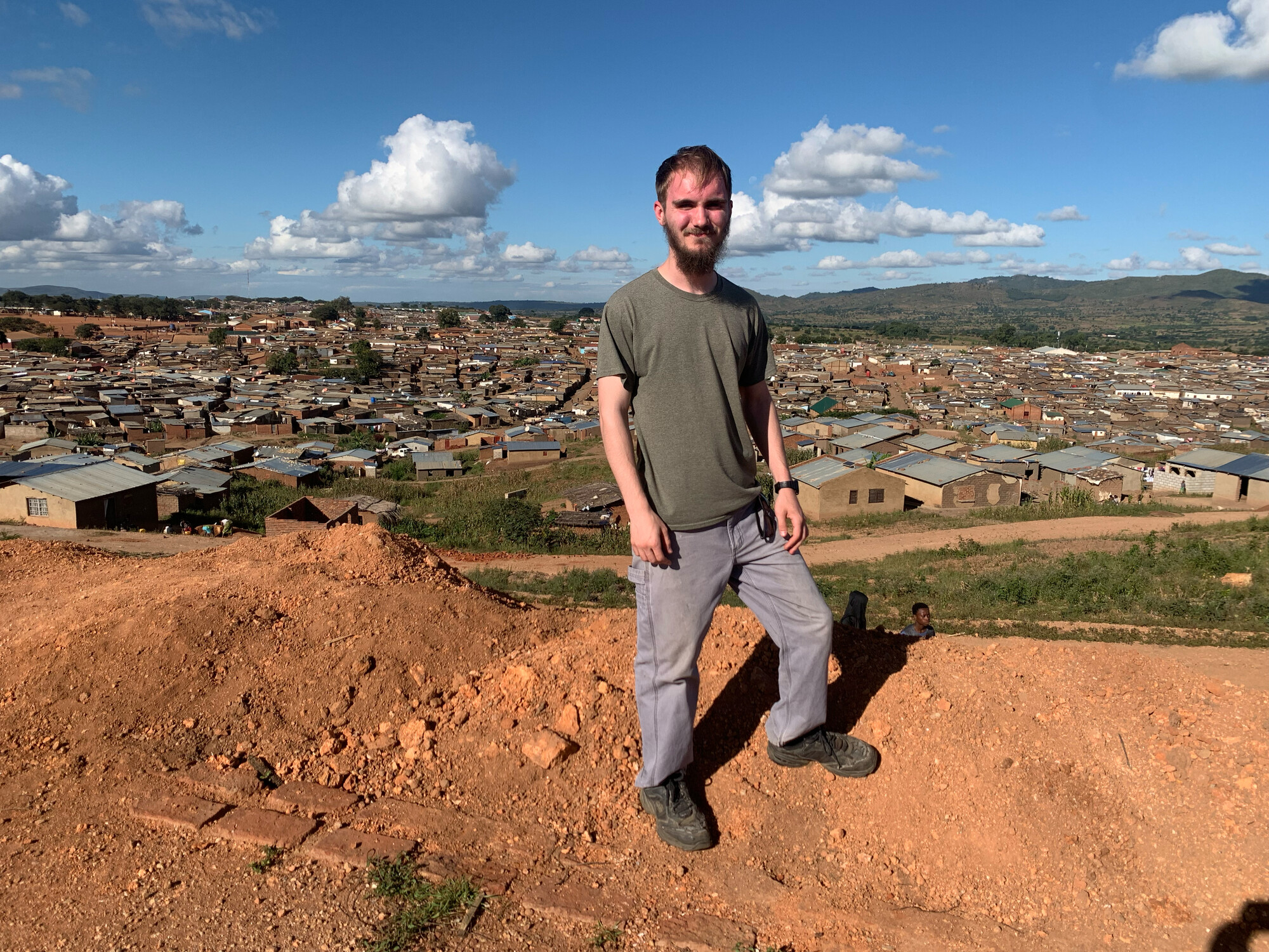 man standing on hilltop with refugee camp behind him