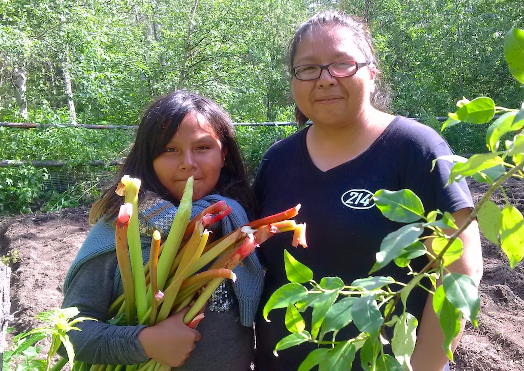 A woman and young girl smile for a photo holding fresh vegetables from a garden.
