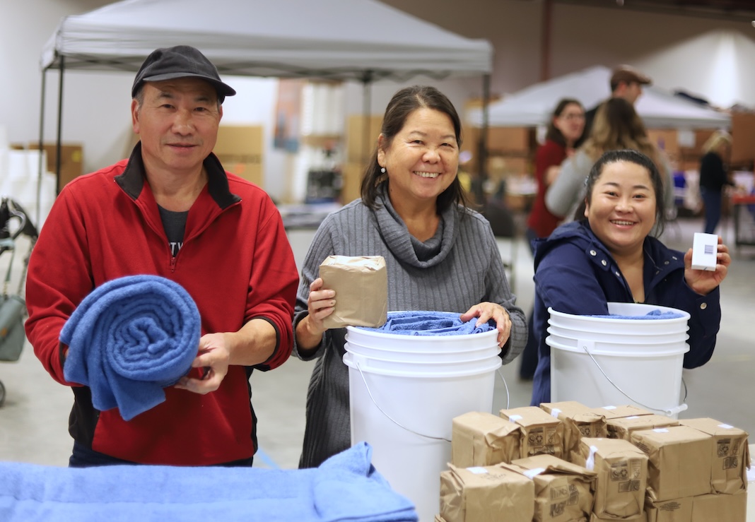 Three people smiling for a photo while packing relief kits.