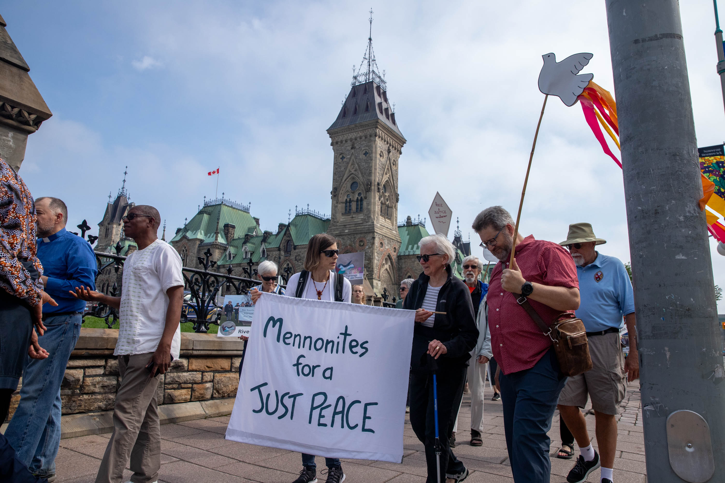 People walk past Parliament hill holding a sign that reads "Mennonites for a just peace"