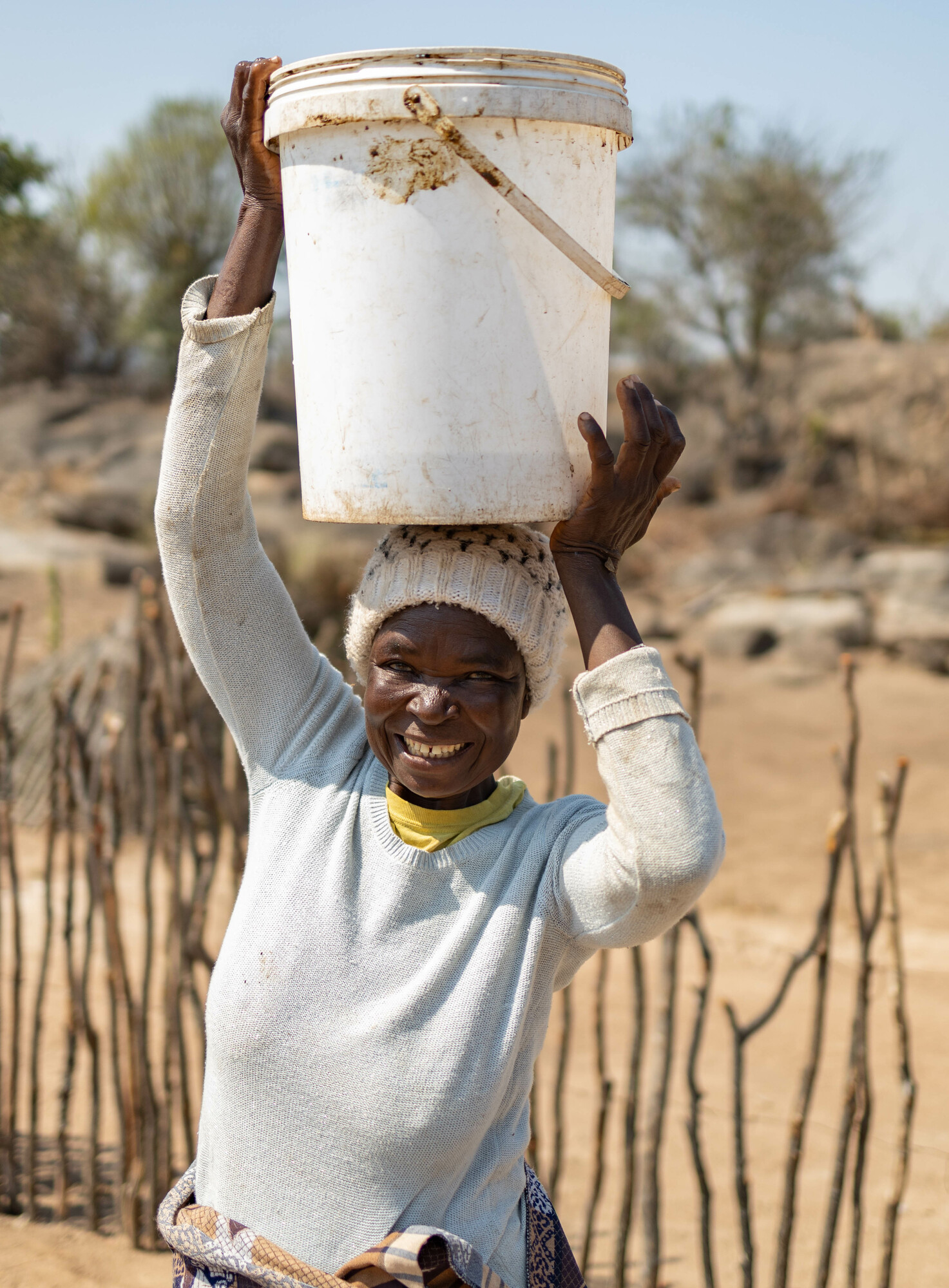 A woman holds an empty pail on her head.