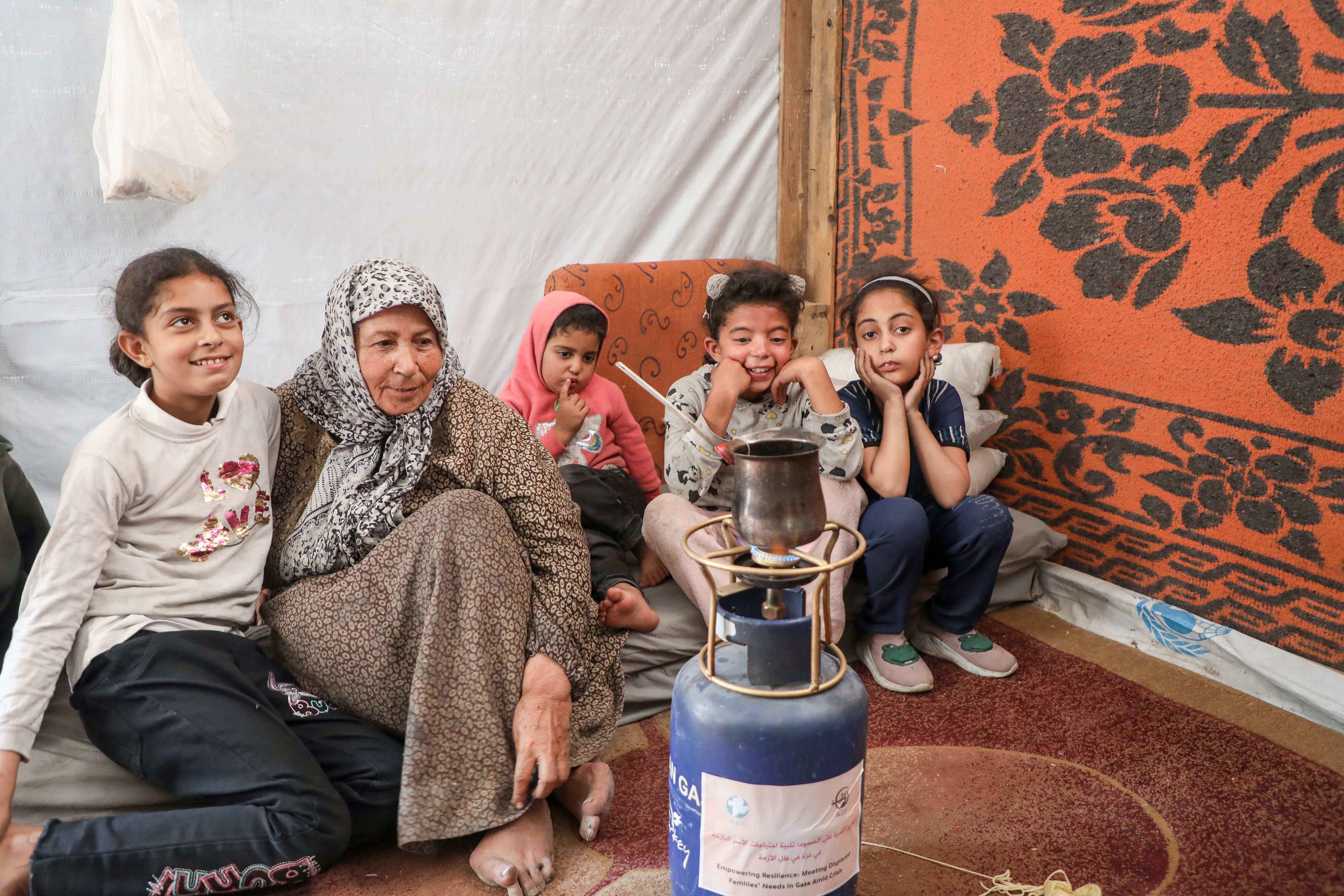 A family that is living in a tent heats water on a new portable gas stove.