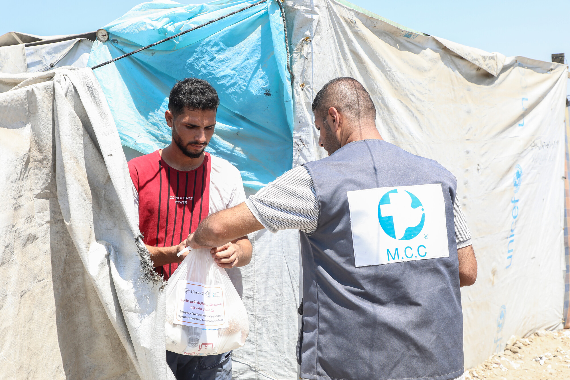 A man wearing an MCC vest hands a bag of food to a man.