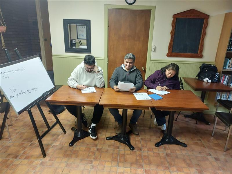 A group of three people sitting at a table signing some paperwork.