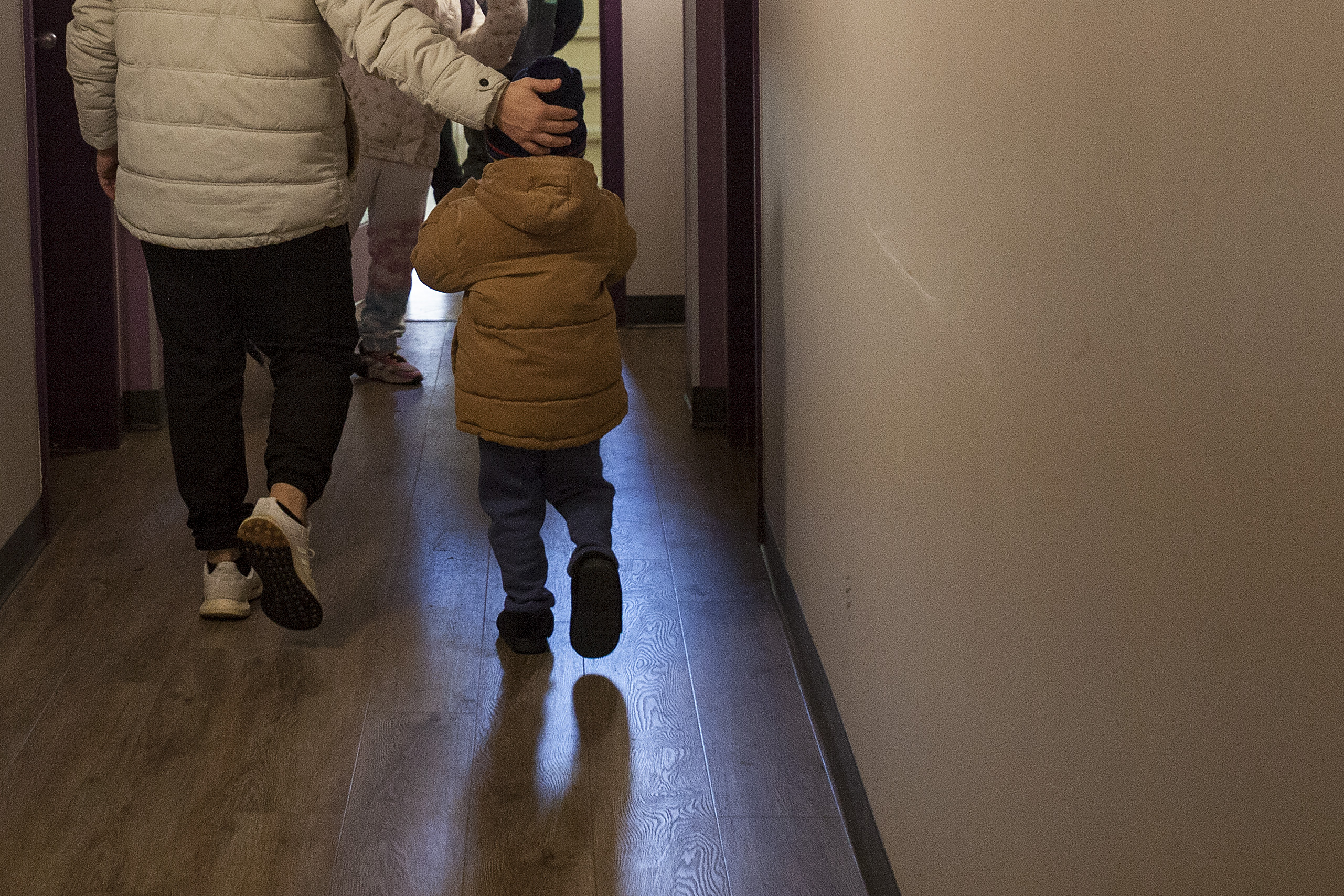 A child in a winter coat runs down a hallway after their parent