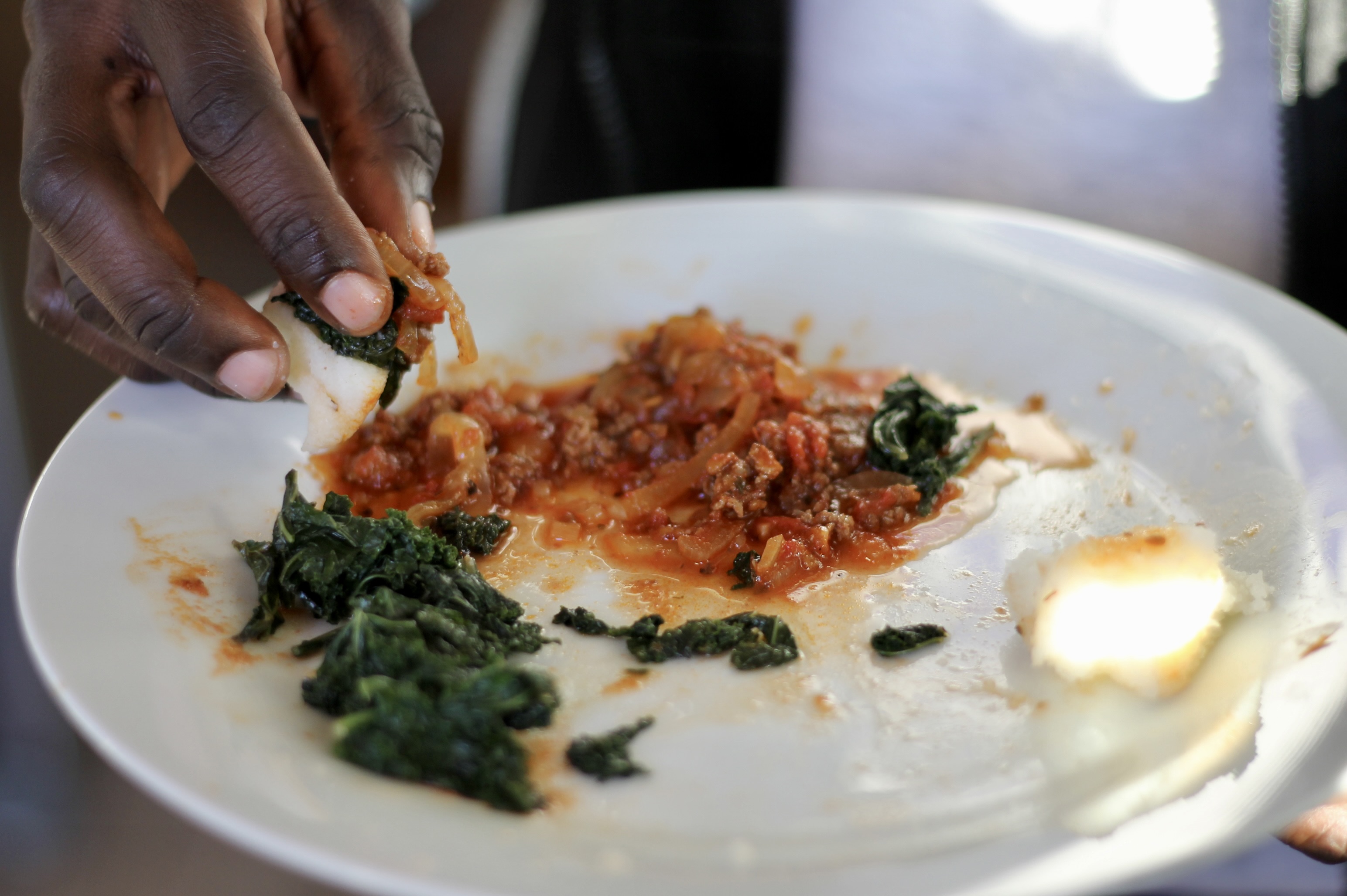 A plate of xima with a tomato-onion gravy and sautéed kale.
