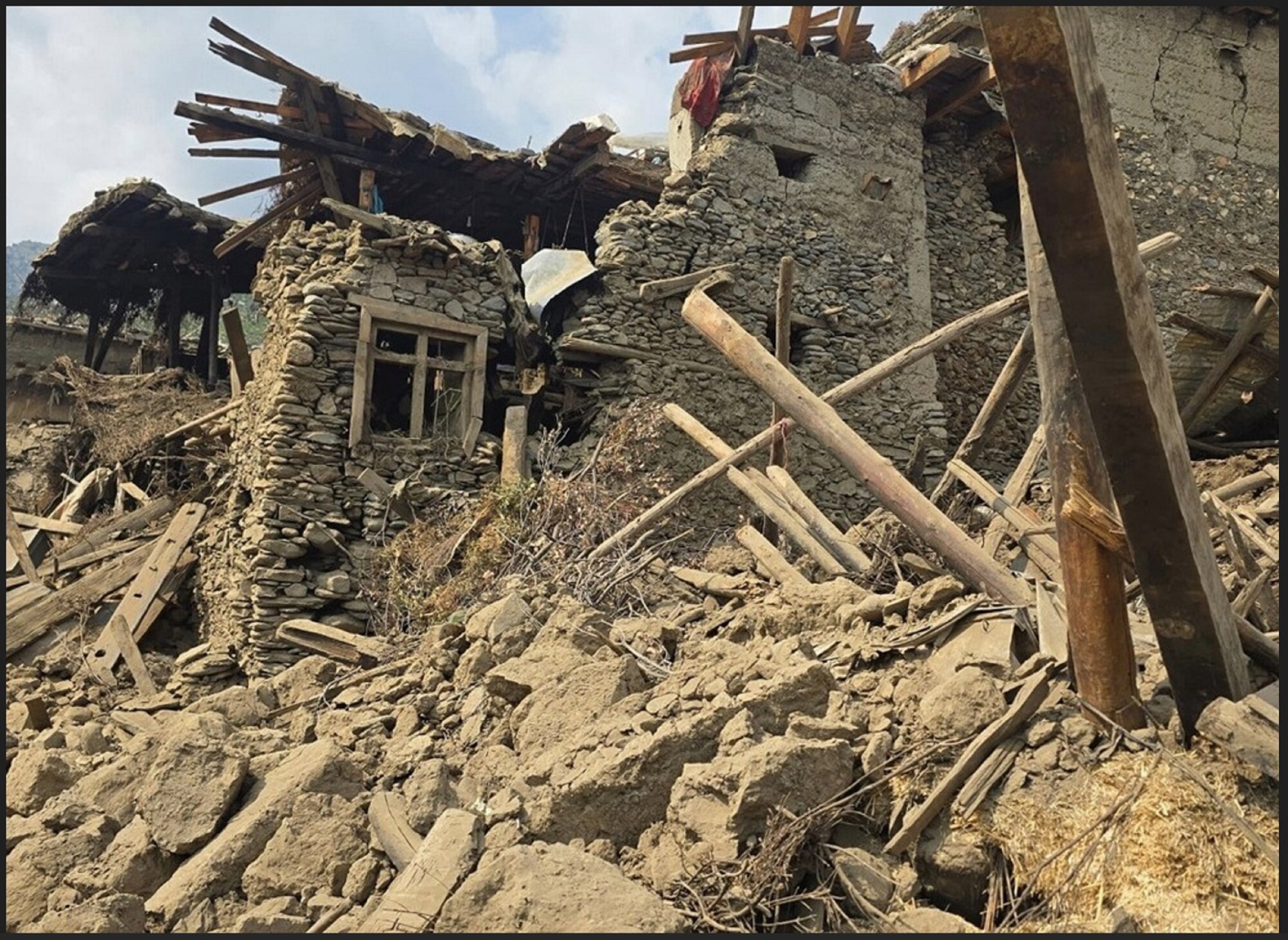 The image shows a collapsed stone structure surrounded by debris, with wooden beams and rubble scattered across the ground.