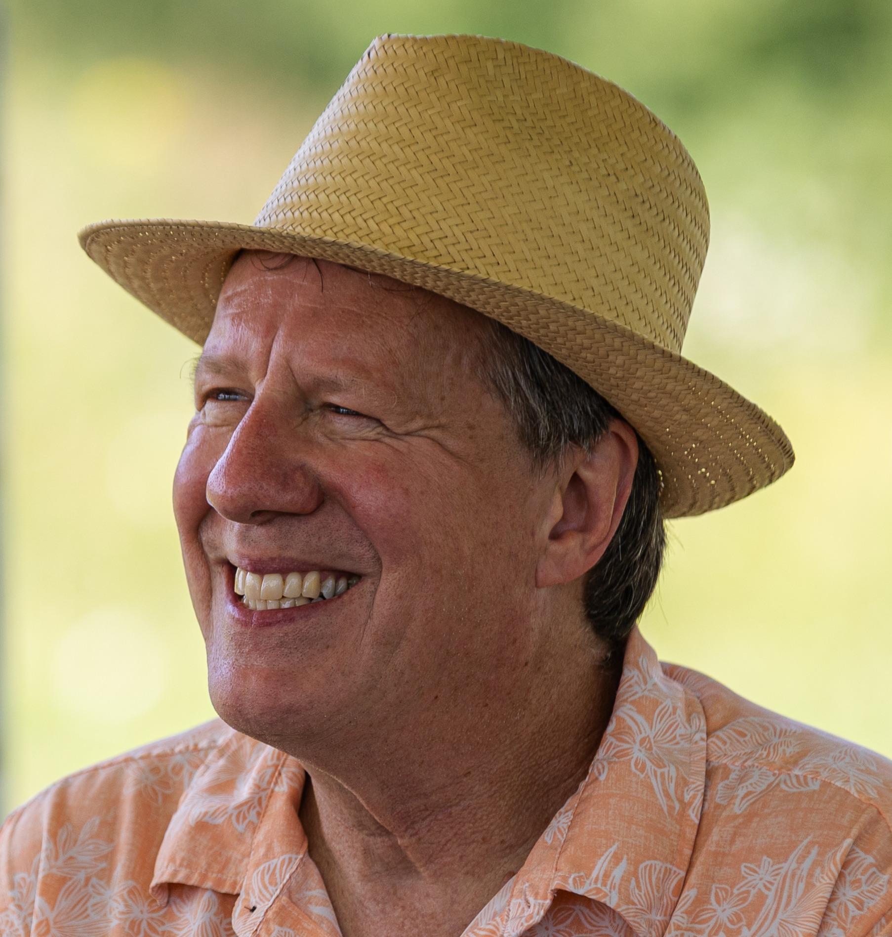 A man smiles wearing a fedora hat and collared shirt.