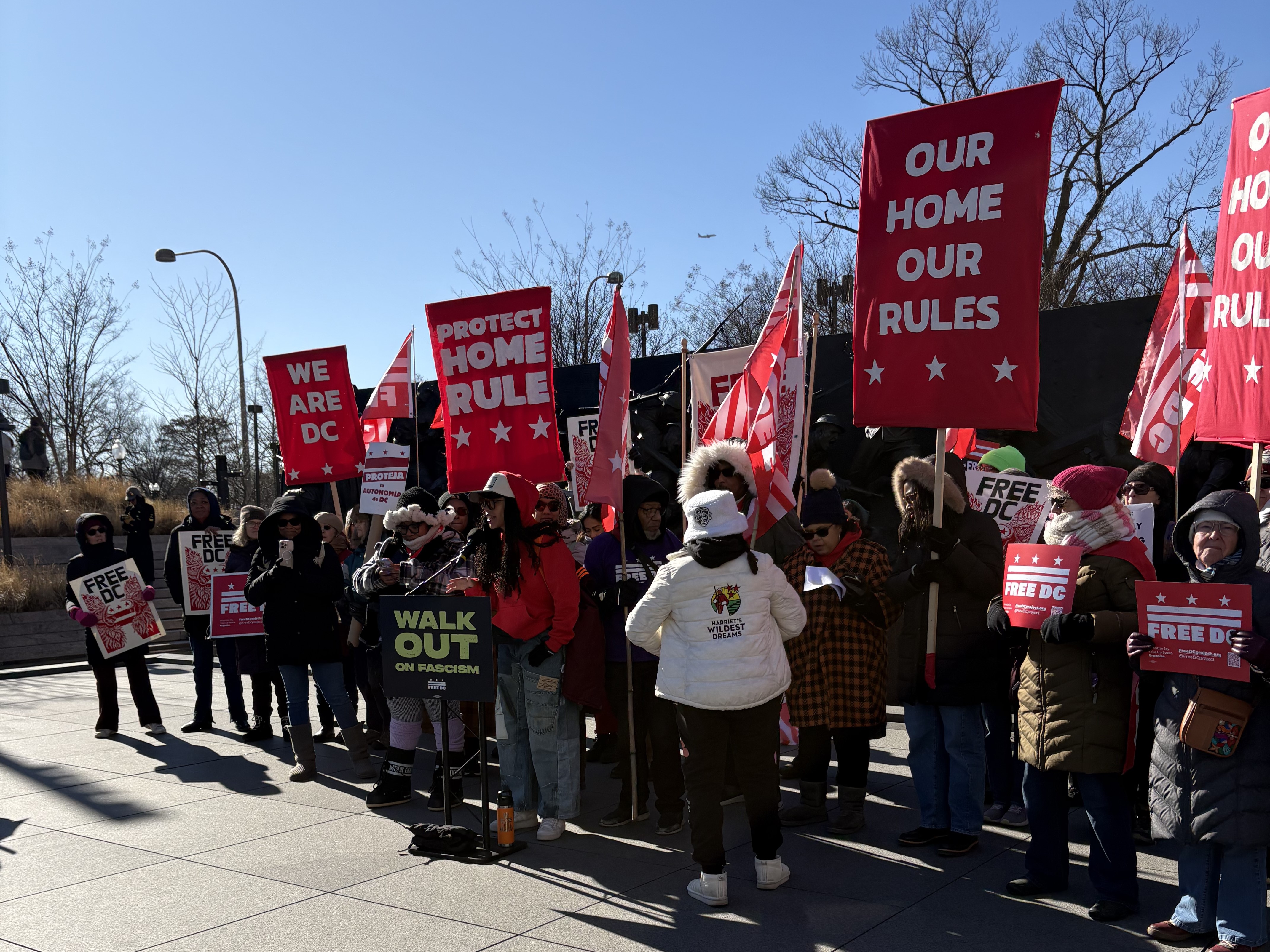 Group of individuals holding protest signs stand outside.