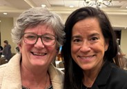 An older woman with grey hair poses next to a younger woman with dark hair.