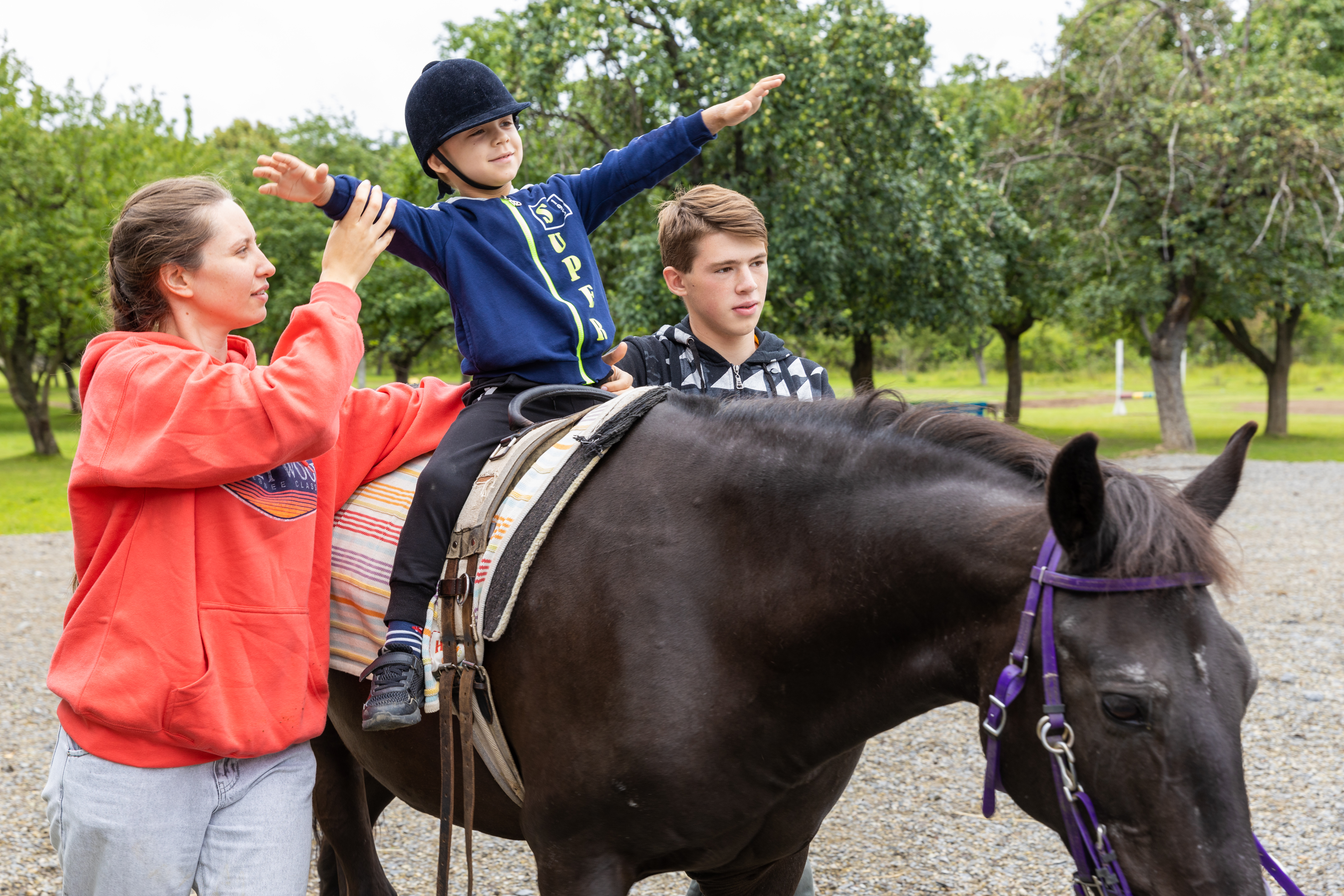 A young boy is helped by two adults to ride horse
