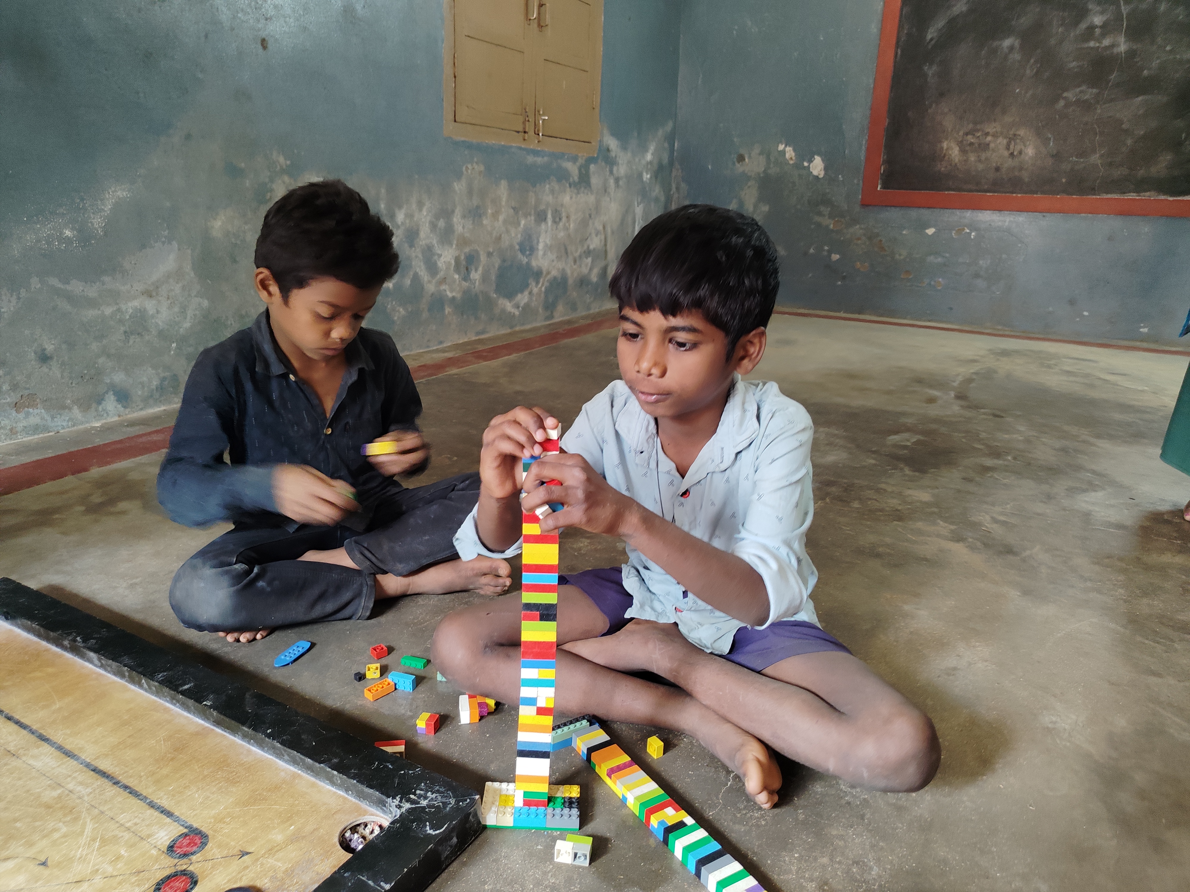Two boys from India play with blocks in a bare room. 