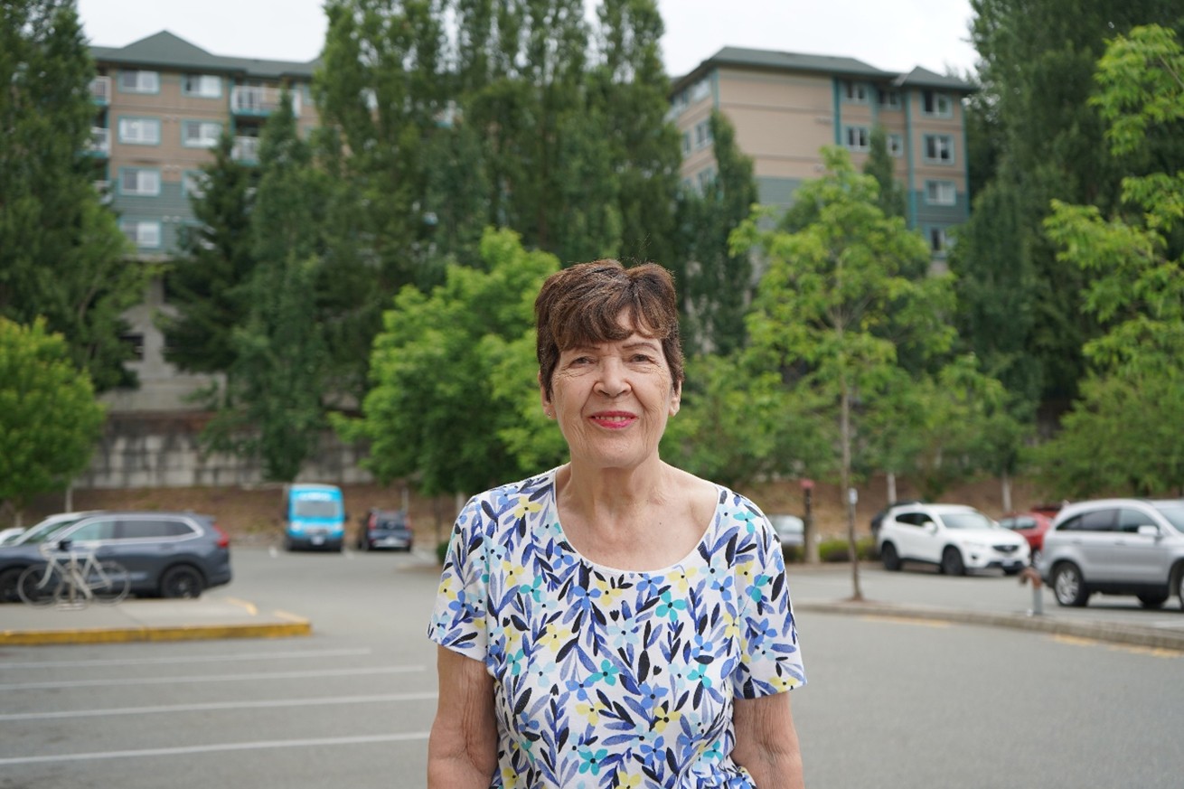 A woman standing in front of apartments smiling for a photo
