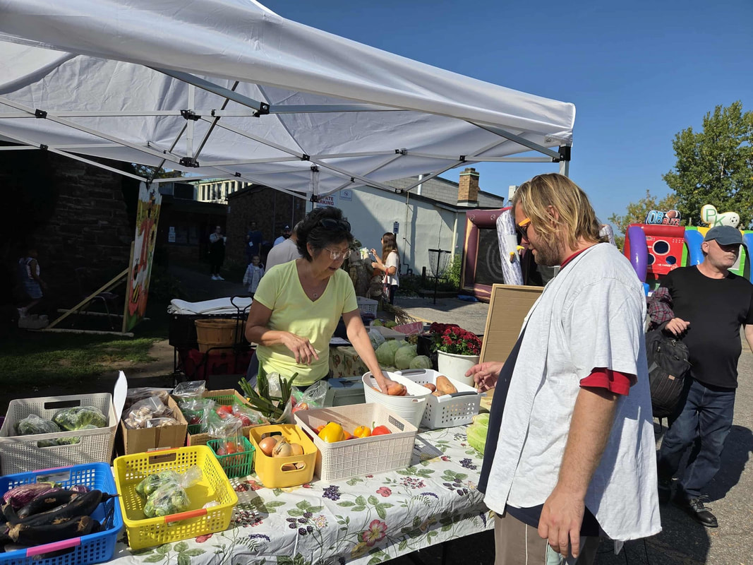A man looks at a table of fresh vegetables as a woman behind the table points at the vegetables.