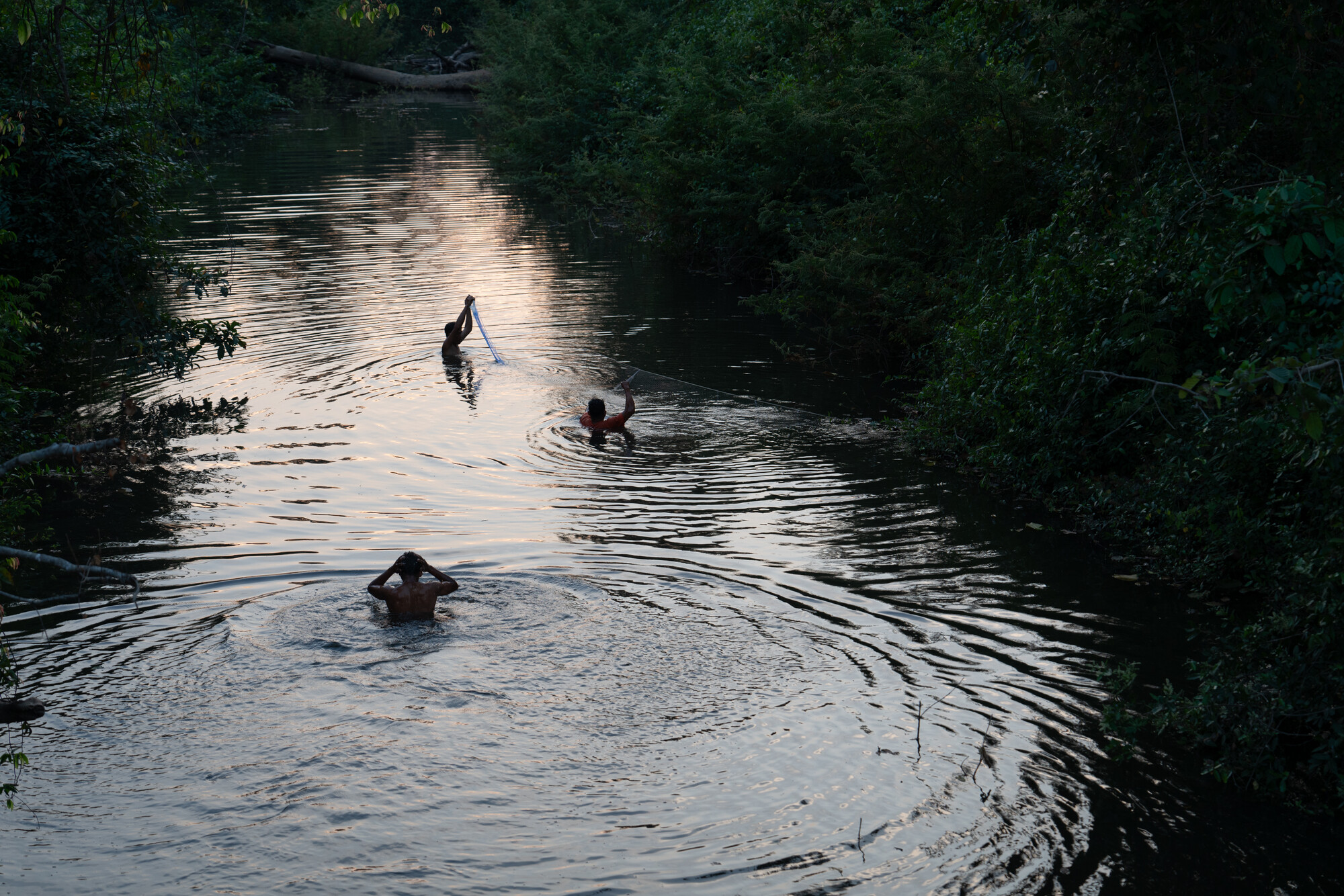 After a day of traveling by motorcycle, forest patrol members  swim and cast fish nets in a local water channel by the forest patrol camp.