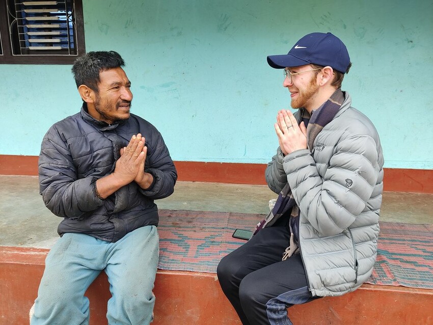 Two people sit facing each other, mirroring body language of hands pressed together in a Nepalese greeting.