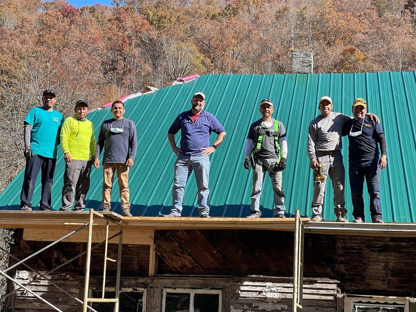 Volunteers from Iglesia Encienda Una Luz in Harrisonburg, Virginia stand on the scaffolding where they have been repairing and adding new metal to the roof of a home near Northfork, West Virginia.