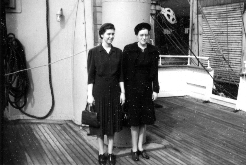 Black and white photo of two women standing together on the deck of a ship. They are smiling.