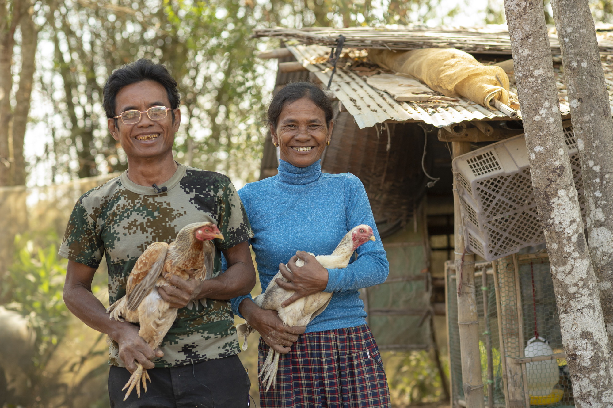 *Chim Yean and his wife, *Reach Koeun, pose with chickens at their farm in the village of Prey Toum. They purchased chickens using interest-free loans from the agriculture cooperative they joined in t