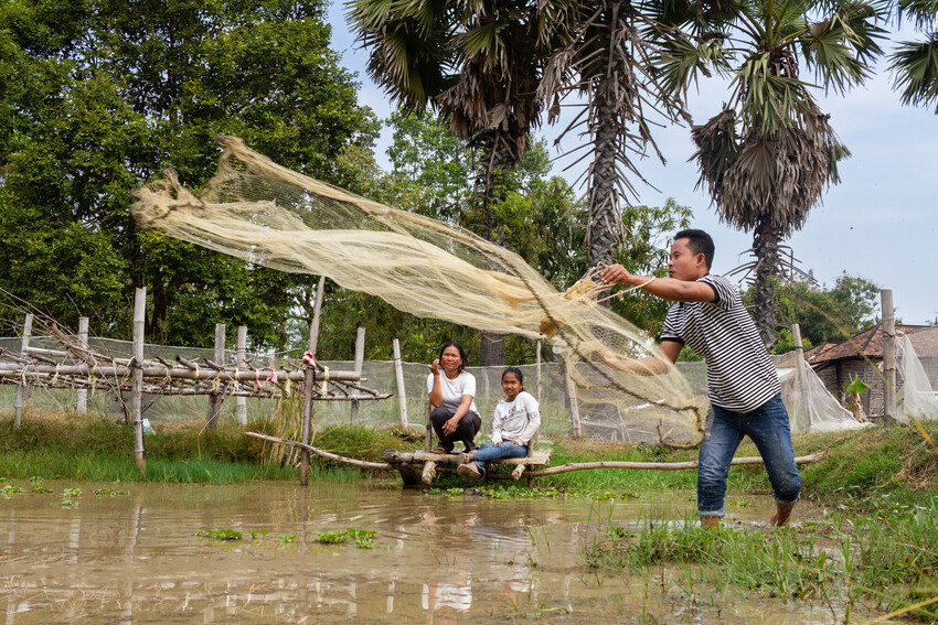 Staff member from MCC partner Organization to Develop Our Villages (ODOV) Nov Dina, throws a net into a fishpond at the farm of ODOV farmer Mok Samun. This demonstration is to show several ODOV projec