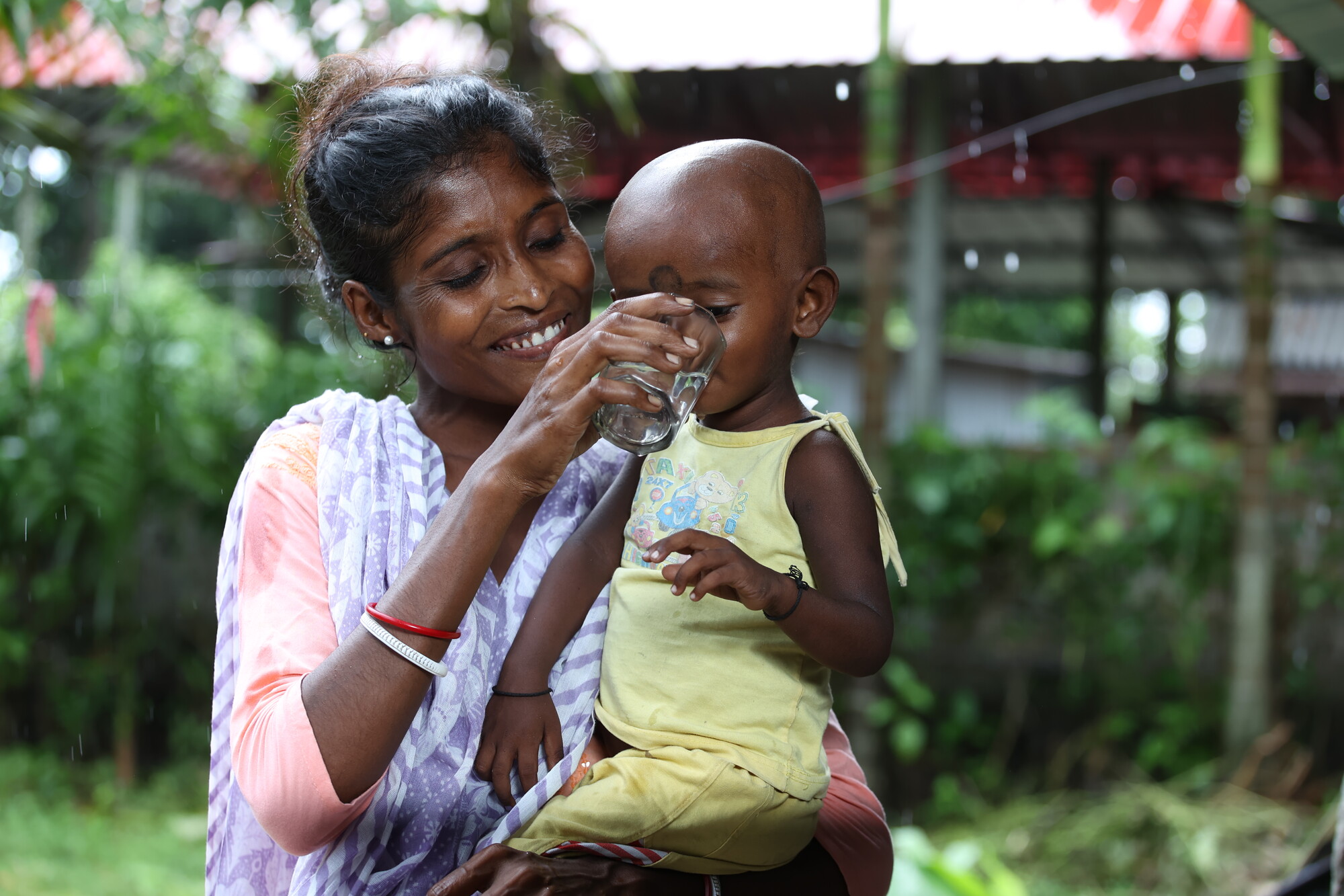 Minati Kerketta helps her son Manab Oraon drink from a cup full of clean water drawn from her Little Flock Fellowship provided water filter.