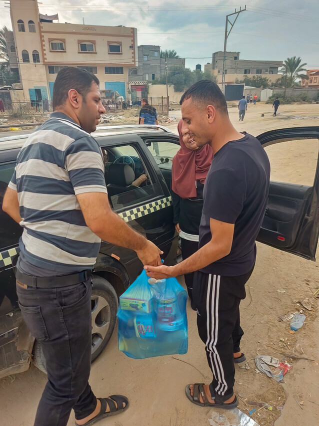 Ahmad Abu Nahel, right, receives a bag full of food from Mohammed Marouf, an Al-Najd Developmental Forum volunteer, while Rifqa Hamalawy, right, an Al-Najd staff member, looks on.