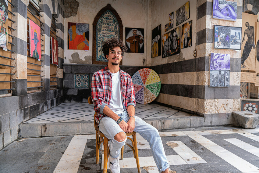 Melad Issa seated in front of the work of Harmony participants at the Beyond Colors exhibition in Homs, Syria, in 2022.