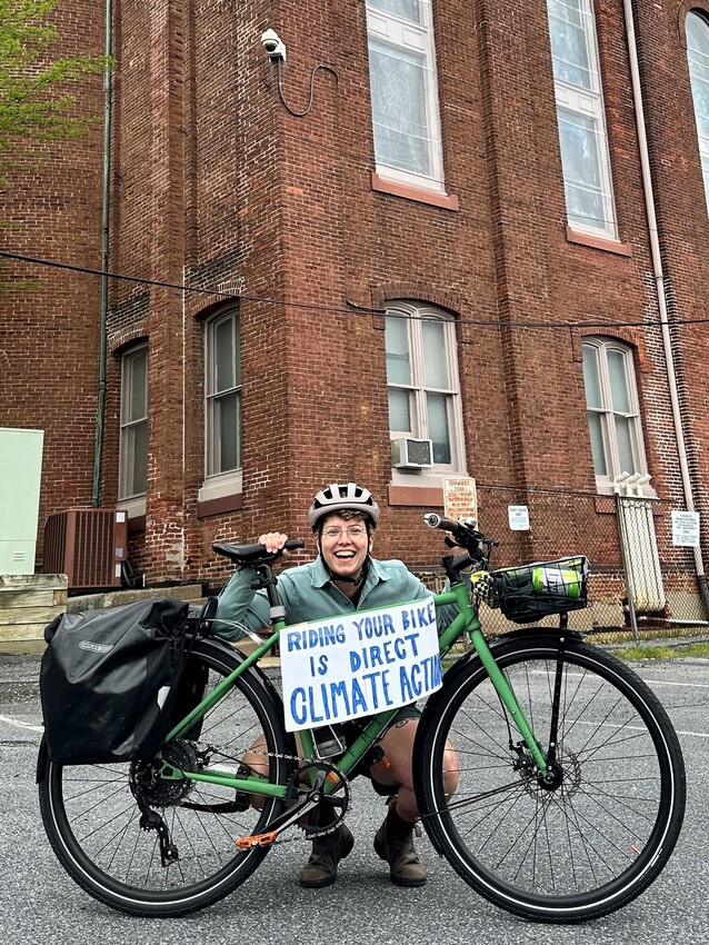 Laura Pauls-Thomas, communications director for MCC East Coast, poses with her bicycle and a sign that says, “Riding your bike is direct climate action” at the Lancaster County Climate Summit on E