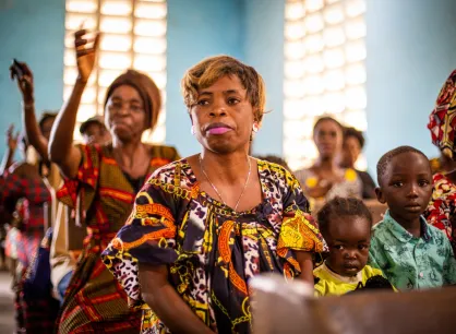 A Congolese woman sits in a church pew. Next to her are two children