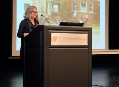 A woman with grey hair speaks in front of a lectern