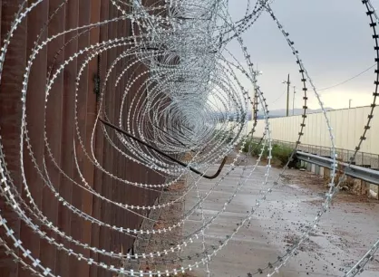microsoftteams-image27_0.png Looking through a coil of barbed wire at a border wall