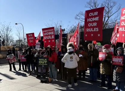 Group of individuals holding protest signs stand outside.