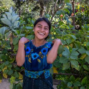 A young woman standing against a leafy background