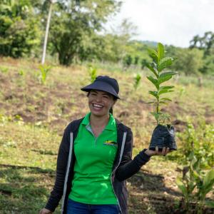 A woman smiling holding up a tree seedling