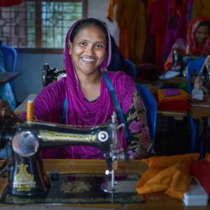 A woman smiling sitting at a sewing machine