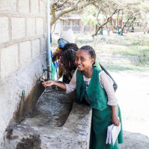 Young children drinking from a faucet at a school