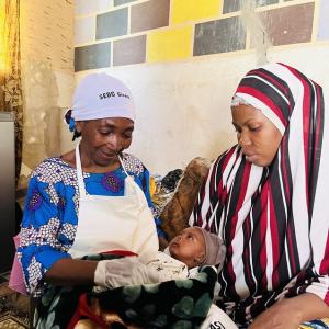 A mother holds her young baby with a doctor sitting next to them performing a check up