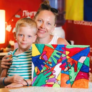 A woman and young boy smile for a photo displaying a piece of art