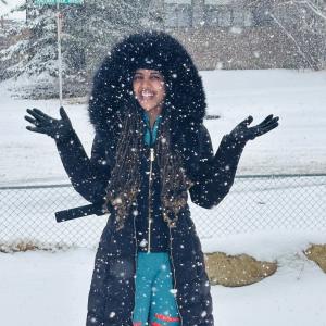 A young woman in a winter coat smiling for a photo with snow in the background