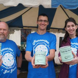 Two men and a woman smiling holding up MCC cans of meat.