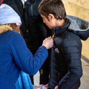 A kid tries on a new coat with assistance from his parent.