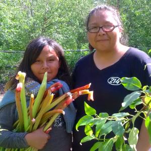 A woman and young girl smile for a photo holding fresh vegetables from a garden.