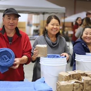 Three people smiling for a photo while packing relief kits.