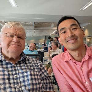 Two people sit next to each other and smile at the camera. One wears a nametag that says "Ken."