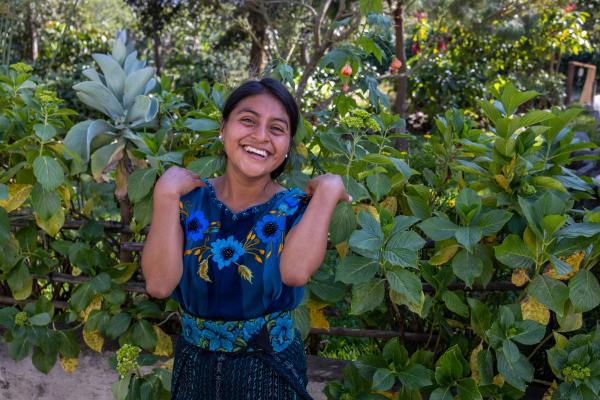 A young woman standing against a leafy background